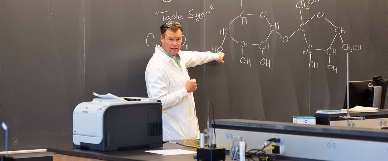  Organic chemistry, Dr. Fennie, pointing to the blackboard while teaching a chemistry class. 