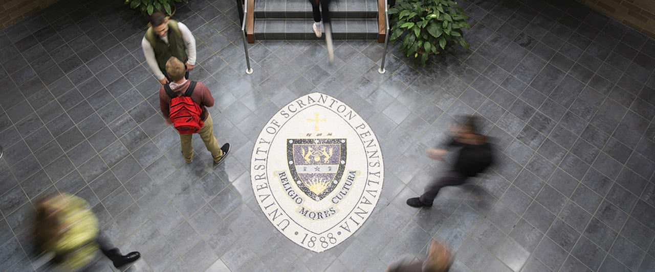  Zoomed in view of people walking past the seals sign on the floor of Brennan Hall.