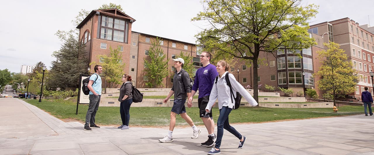  Students walking and stopping to talk in front of Gavigan Hall, a sophomore year on-campus housing hall. 