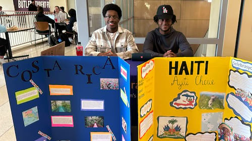 Two students seated behind a table and brightly-colored trifold posters.